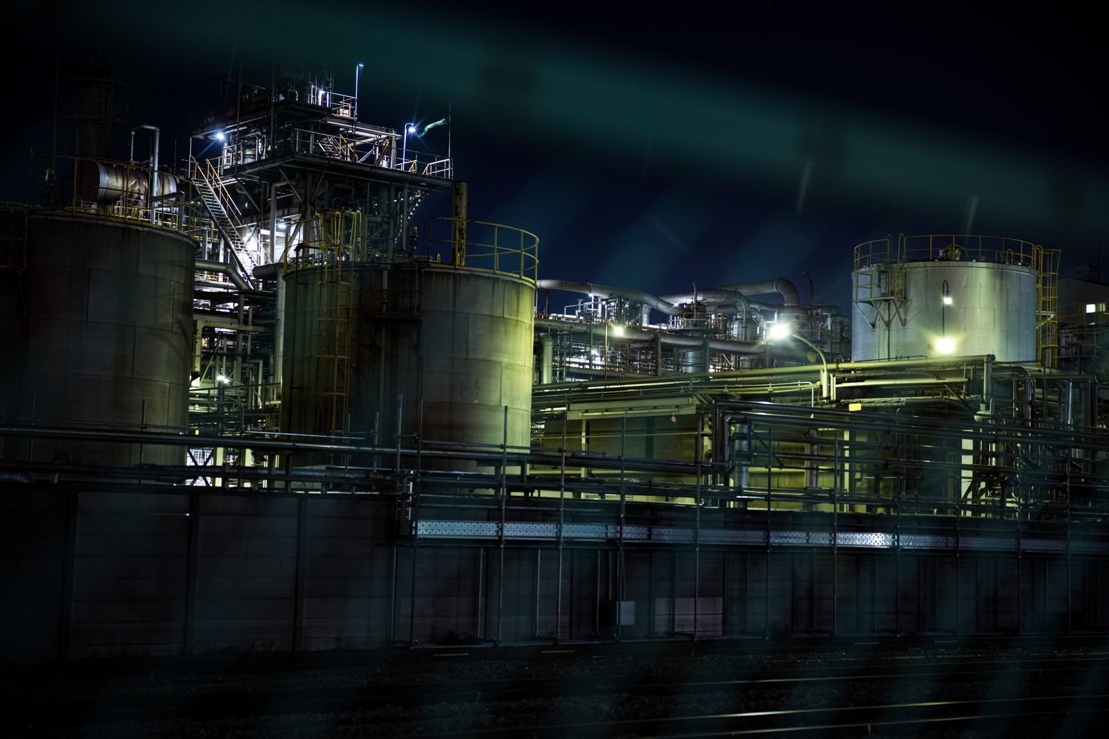 「フェンス越しに浮かび上がる工場夜景」の写真