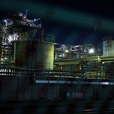 フェンス越しに浮かび上がる工場夜景の写真