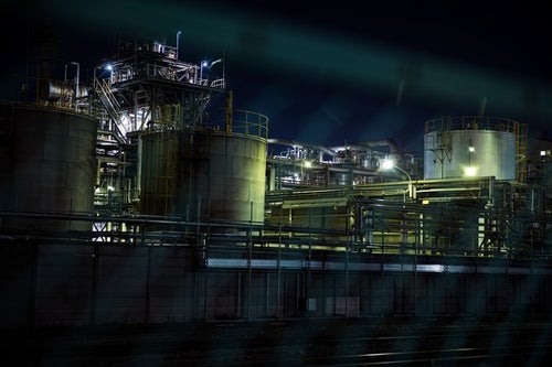 フェンス越しに浮かび上がる工場夜景の写真