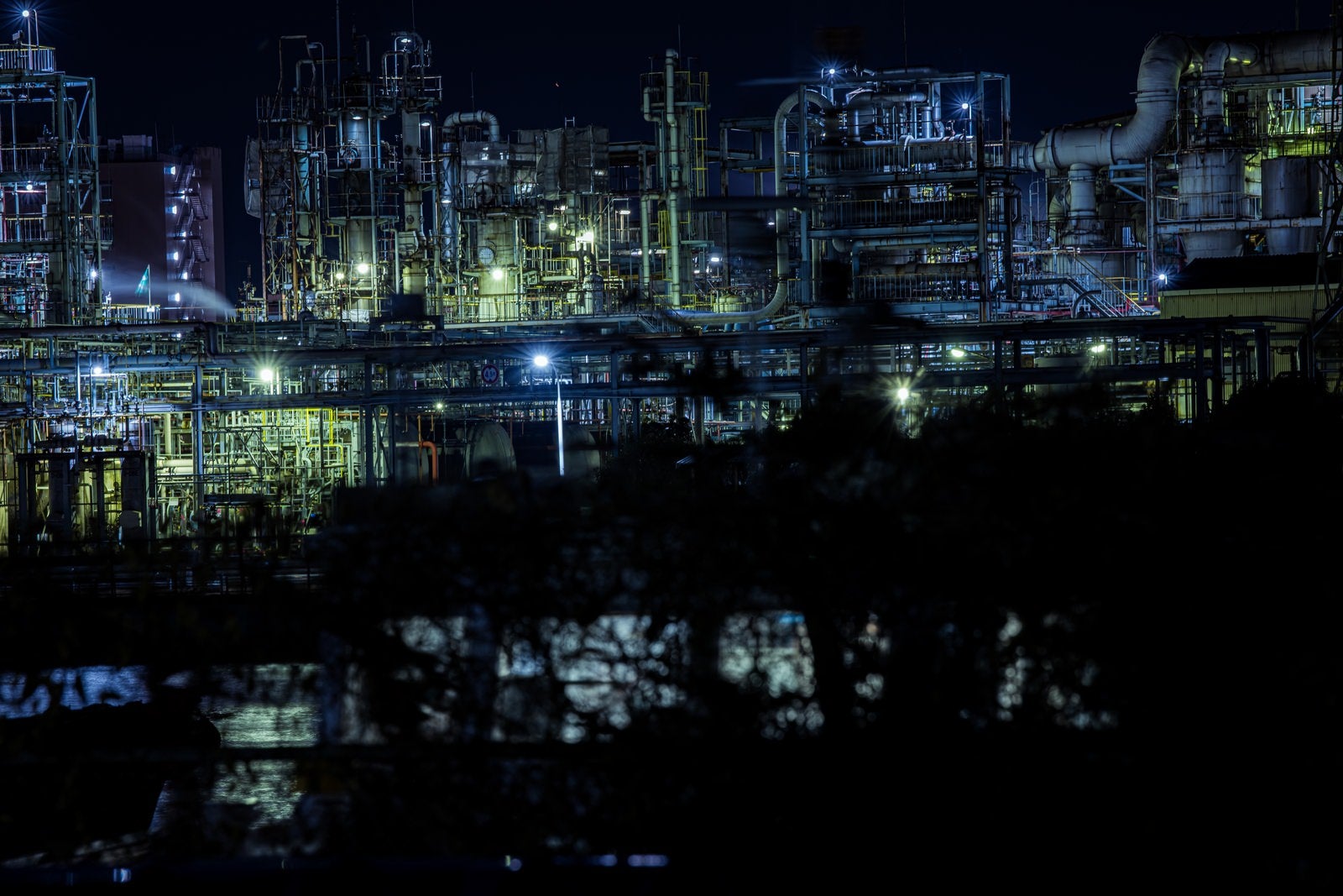 「木々の陰から浮かび上がる工場夜景」の写真