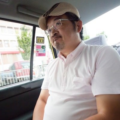 タクシーの運転手に丸くなったと言われて苦笑いをするハンチング帽の男性の写真