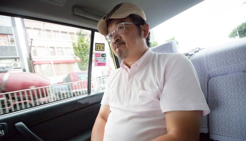 タクシーの運転手に丸くなったと言われて苦笑いをするハンチング帽の男性の写真