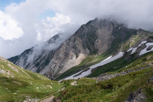 白馬岳（しろうまだけ）の雪渓と沸き立つ雲間に見える山々（白馬岳）の写真