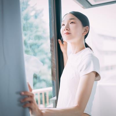 カーテンを開けて爽やかな朝日と自然光を取り入れる女性の素材