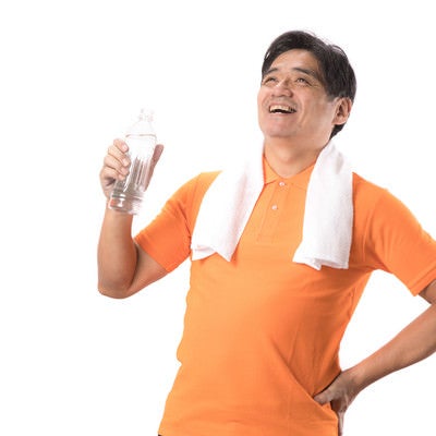 軽い運動後にペットボトルの水を飲む中年男性の写真