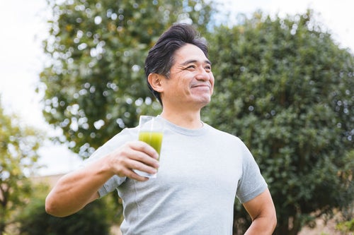 青汁が入ったコップを握りしめる健康体の中年男性の写真