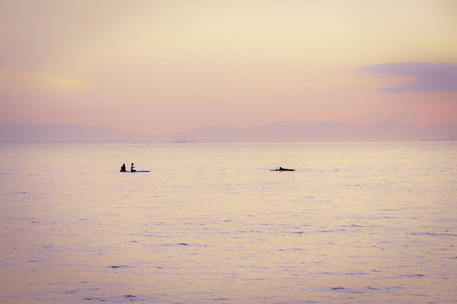 「夕暮れに染まる静かな海上とSUPやサーファーのシルエット」の写真