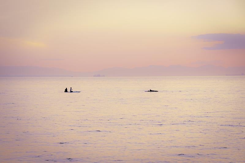 夕暮れに染まる静かな海上とSUPやサーファーのシルエットの写真