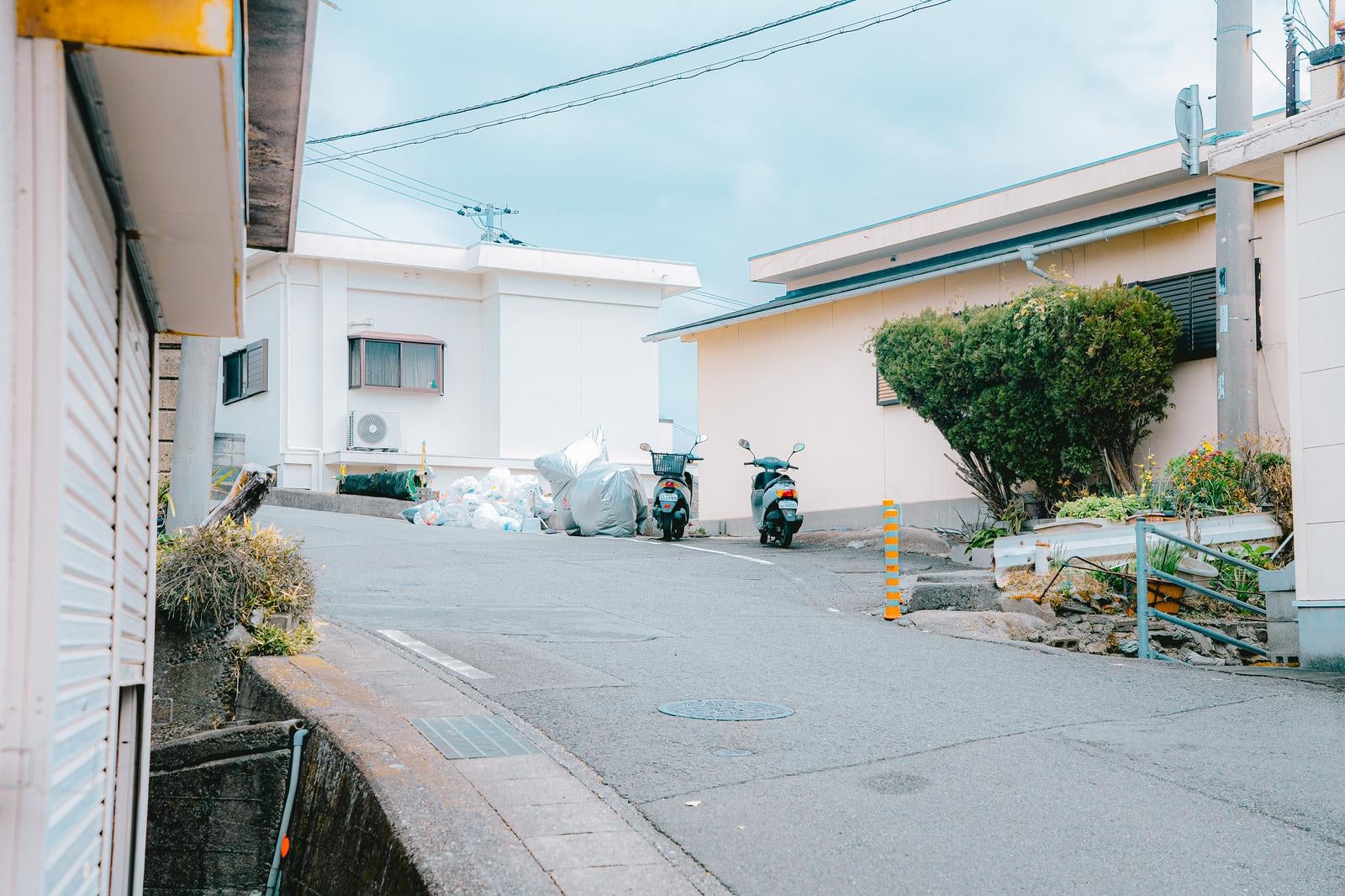 「坂道の道路脇に2台のスクーターが停まる風景」の写真