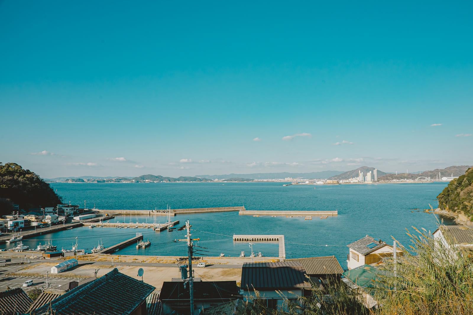 「静かな海と遠くに広がる都市の景色（和歌山県塩津漁港）」の写真