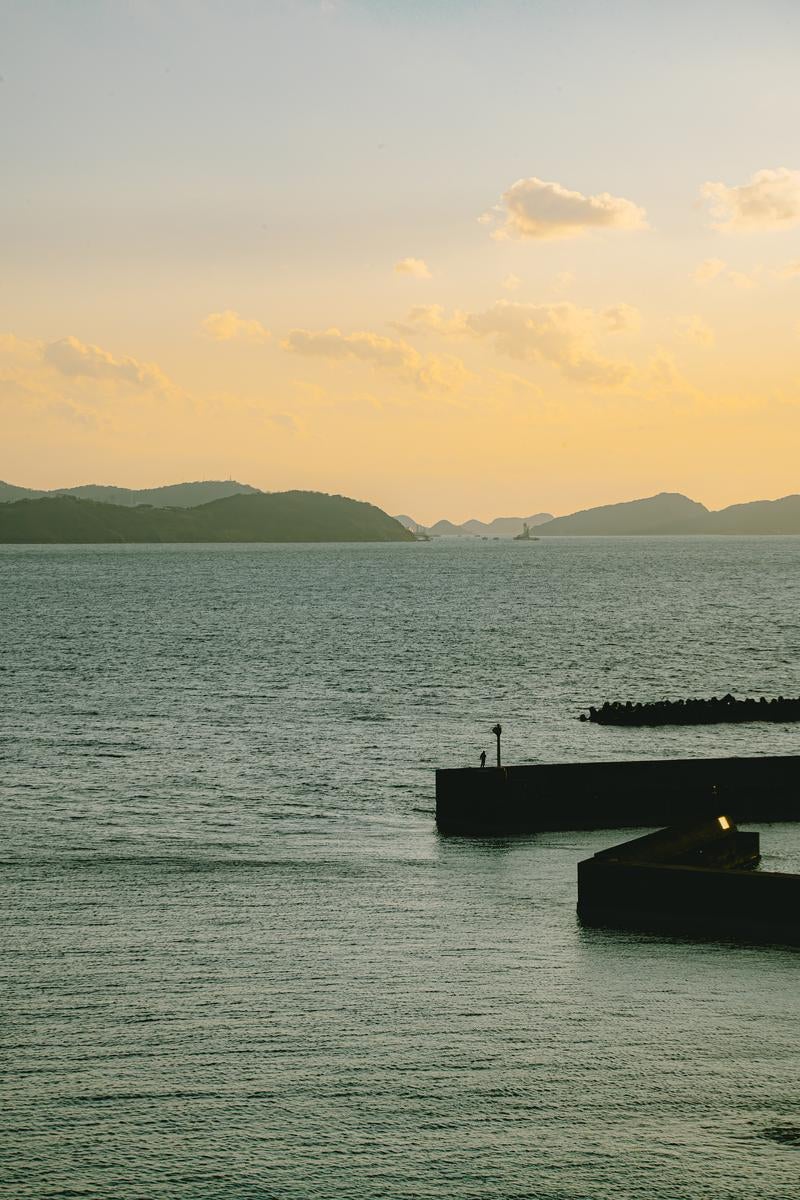 「和歌山県和歌浦の堤防沿いに佇む人と夕焼けの景色」の写真