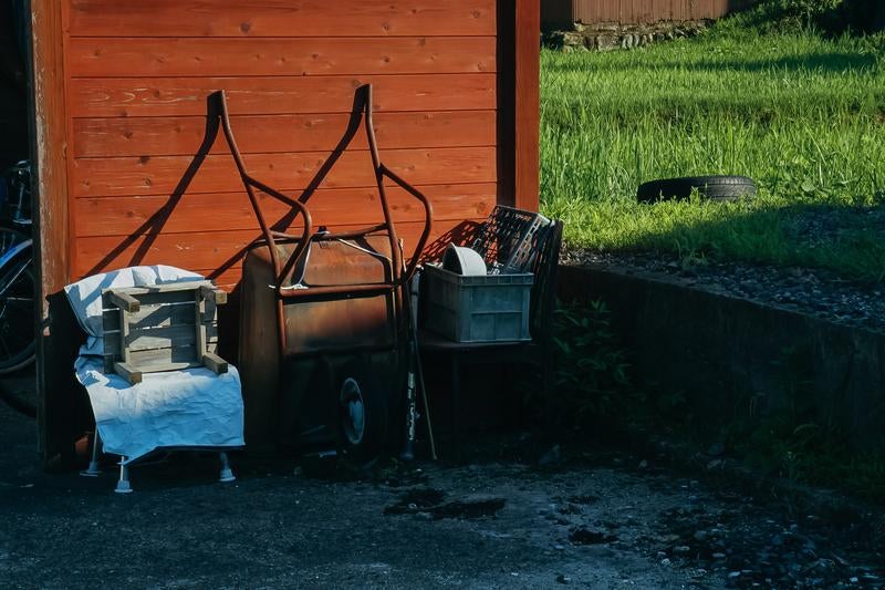 農機具置き場の壁の前にある古い一輪車や木箱の写真