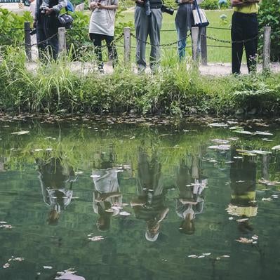 水面に反射する池の前に立つカメコを持つ観光客の姿の写真