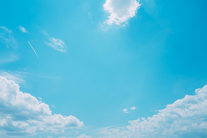 青空に浮かぶ白い雲と飛行機雲の写真