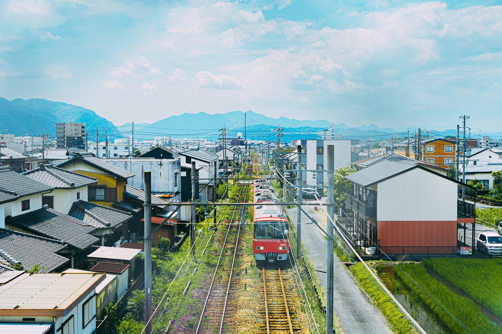 「市街地の線路を進む赤い電車と住宅街の景色」の写真