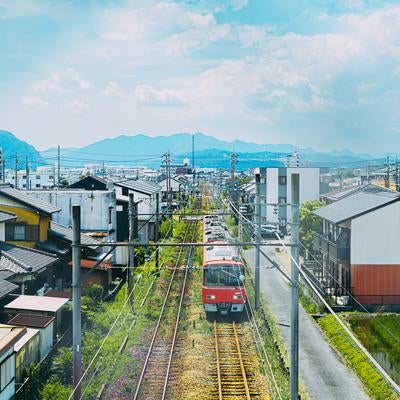市街地の線路を進む赤い電車と住宅街の景色の写真