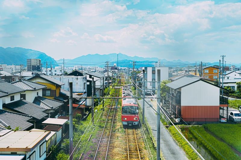 市街地の線路を進む赤い電車と住宅街の景色の写真