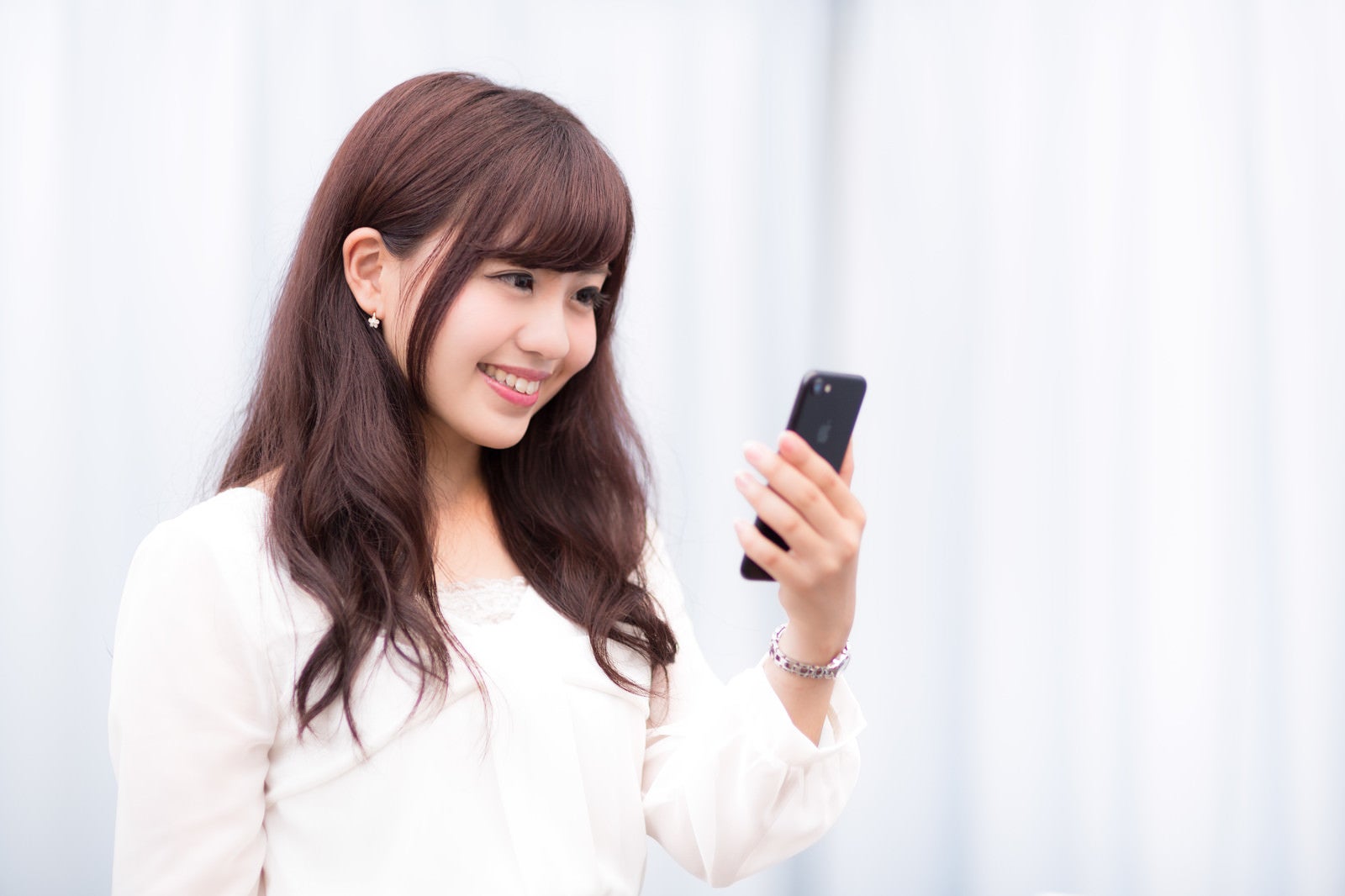 「新しいスマートフォンの高色域ディスプレイにご満悦のキラキラ女性」の写真［モデル：河村友歌］