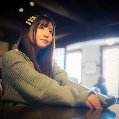 昼間のカフェで窓からの光を浴びながら思案に耽る女性の写真