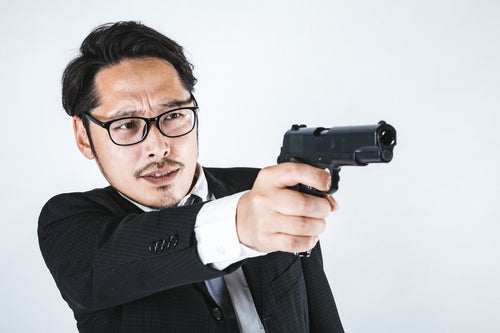 ガン・フーアクション風に拳銃を構えるスーツ姿の男性の写真