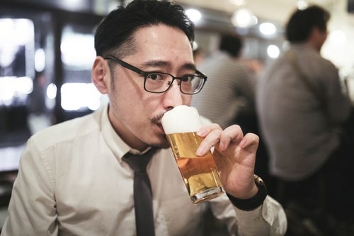 乾杯前にこっそり飲む男性の写真