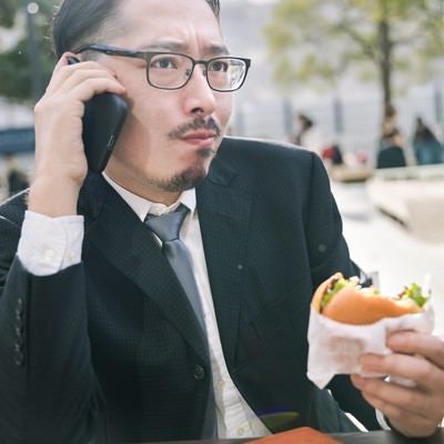 食事中もスマートフォンが手放せないビジネスマンの写真