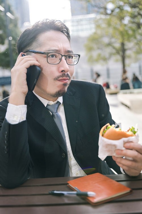 食事中もスマートフォンが手放せないビジネスマンの写真