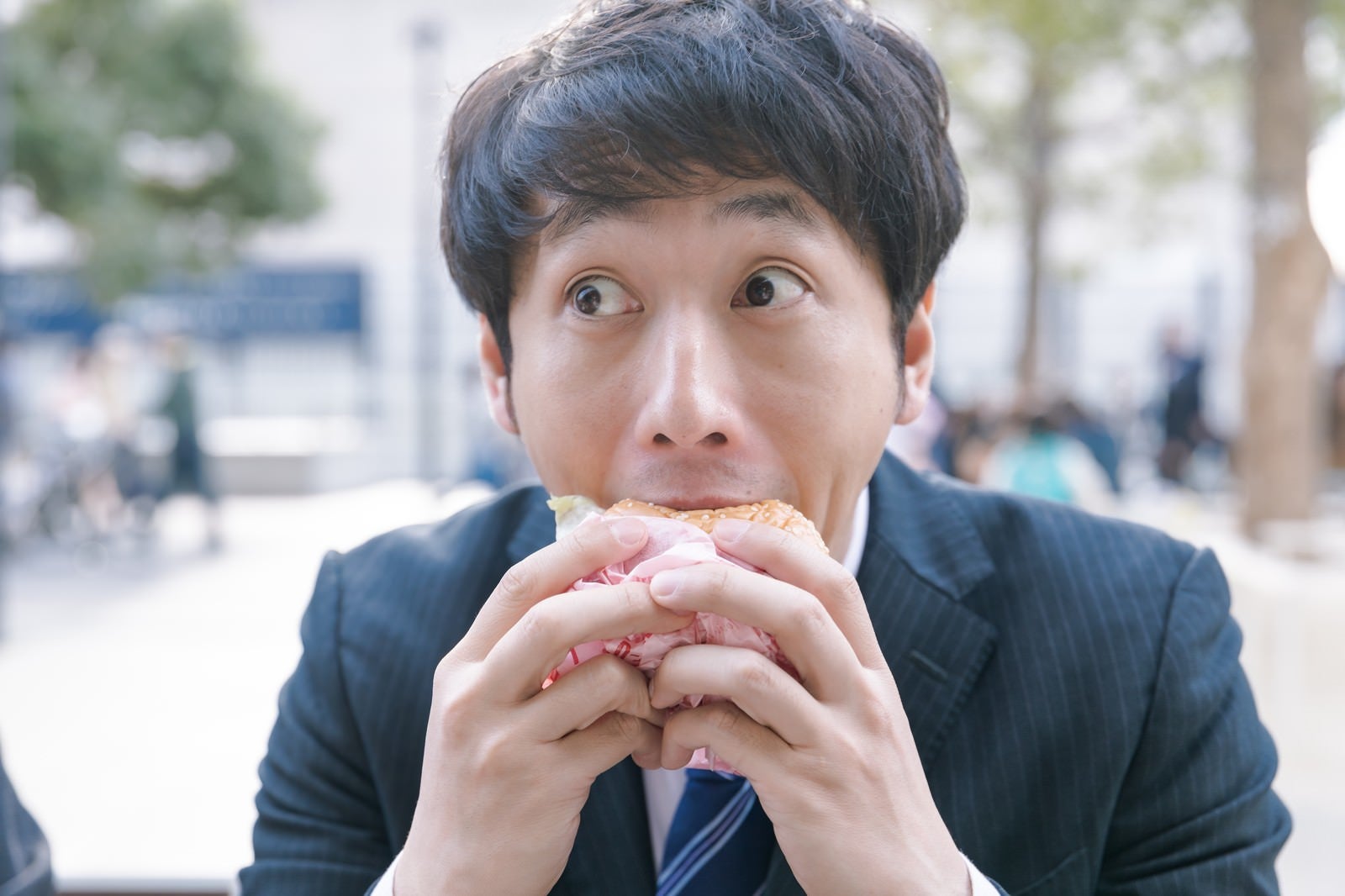 「一心不乱にハンバーガーにかぶりつく会社員」の写真［モデル：大川竜弥］