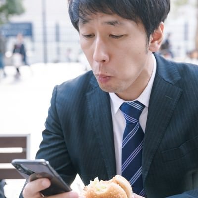 忙しなくランチにハンバーガーを食べる男性会社員の写真