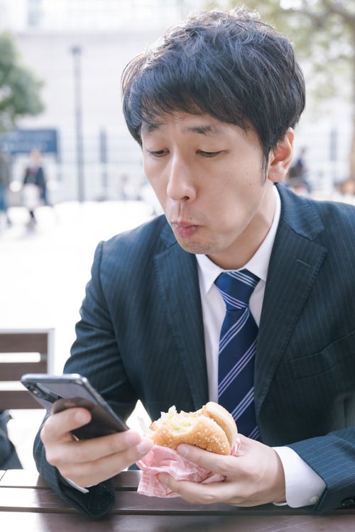 忙しなくランチにハンバーガーを食べる男性会社員の写真