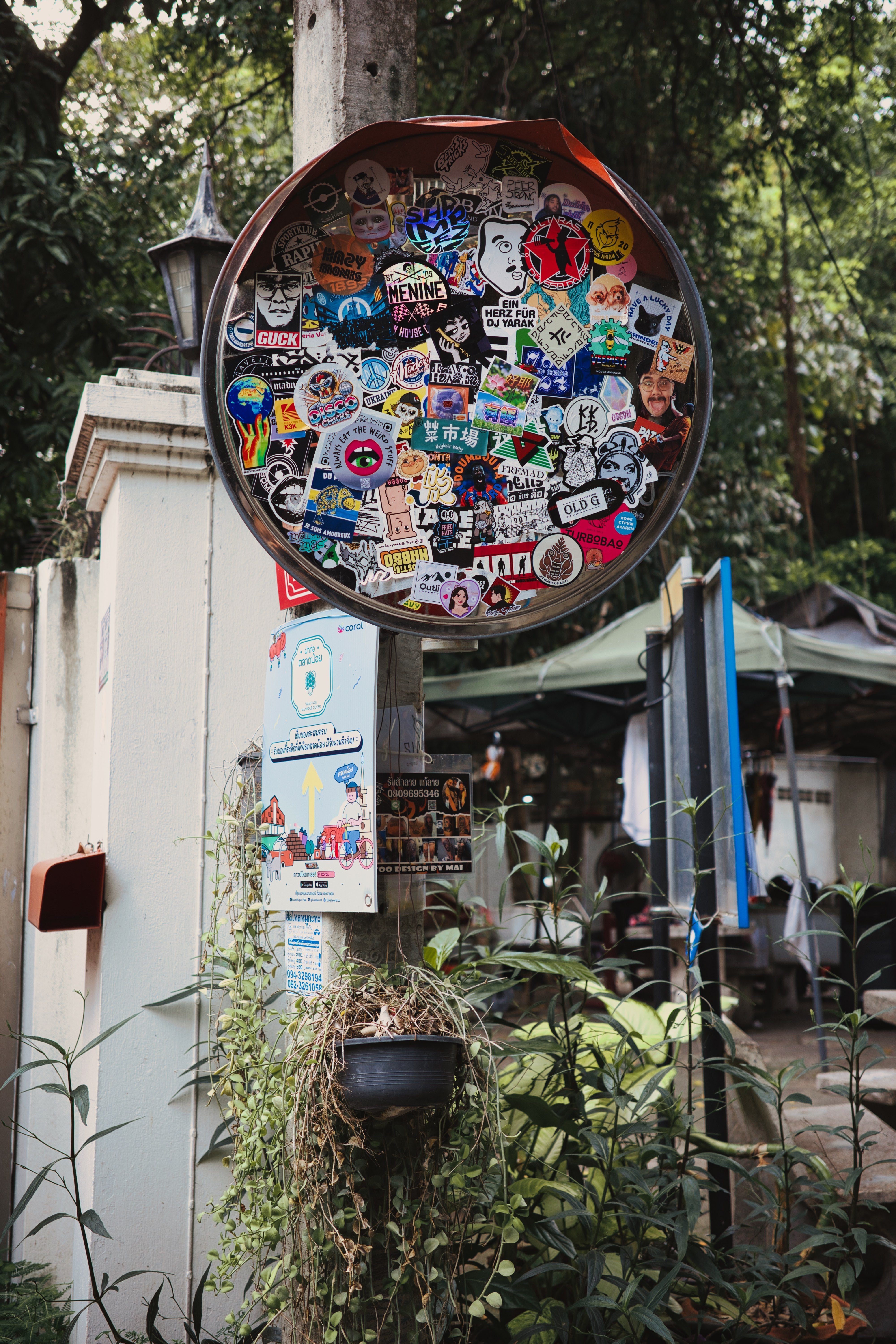 路地裏を彩るステッカーで覆われたカーブミラーの写真