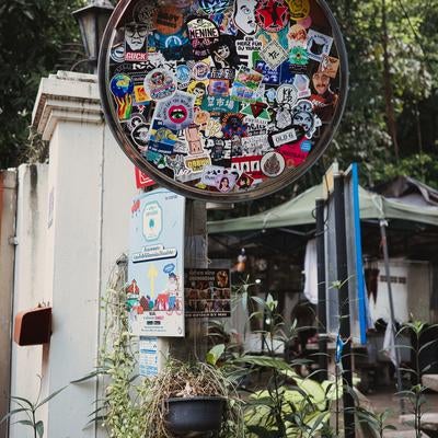 路地裏を彩るステッカーで覆われたカーブミラーの写真
