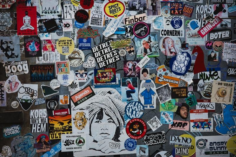 カラフルで隙間なく重なった数百枚のステッカーとシールの密集コラージュ壁面の写真