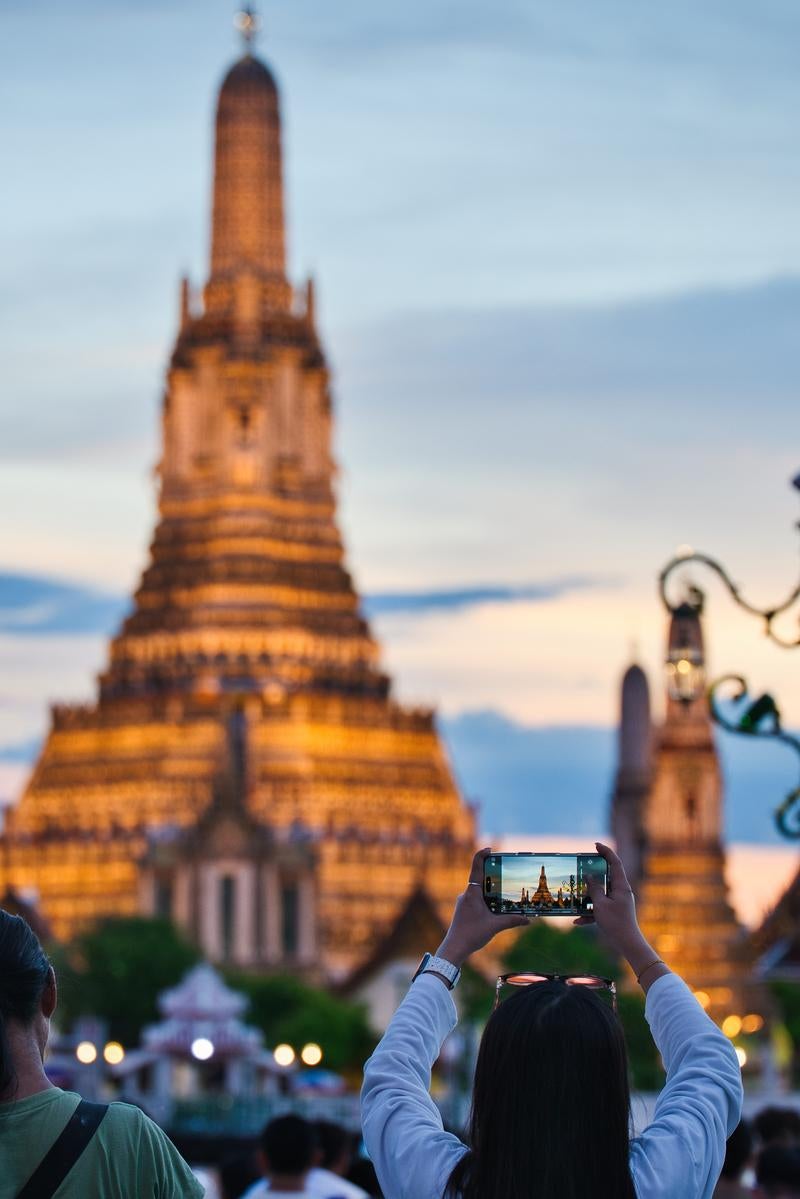 夕暮れのワット・アルンをスマートフォンで撮影する観光客