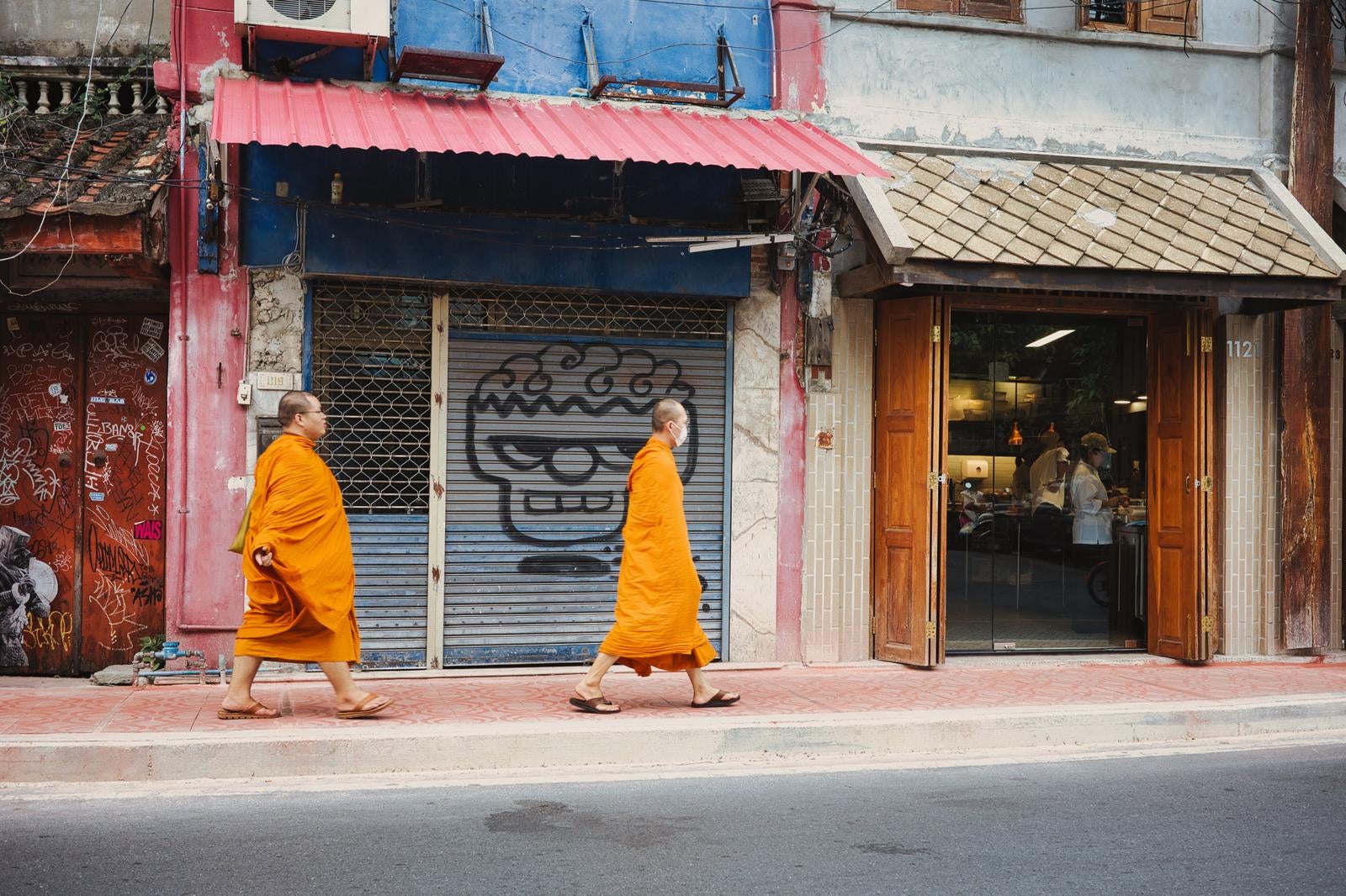 オレンジ色の袈裟を着た二人の僧侶が街の歩道を歩いている