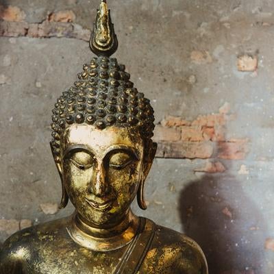 古いレンガ壁の前に置かれた金箔仏像の上半身の写真