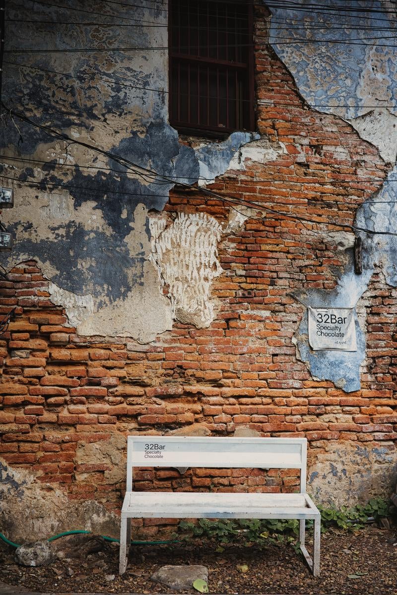 剥がれた塗装の壁面と白いベンチの写真