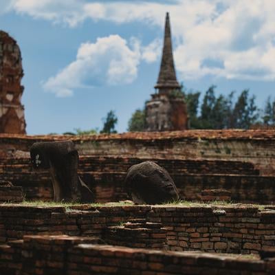 青空の下に横たわる風化した仏頭と赤茶色のレンガ遺跡の写真