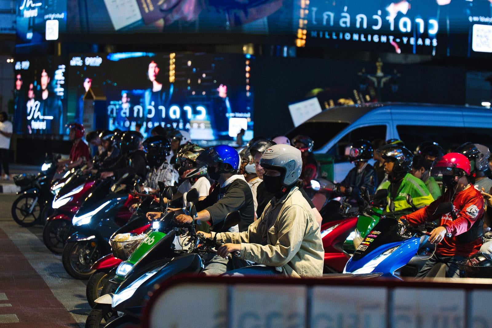 夜の街で信号待ちをする多数のスクーターとライダーたち