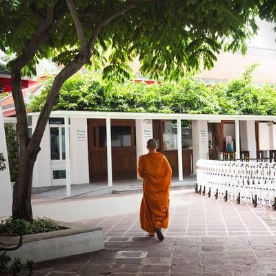 オレンジ色の袈裟を着た僧侶が寺院の中庭を歩く境内風景の写真