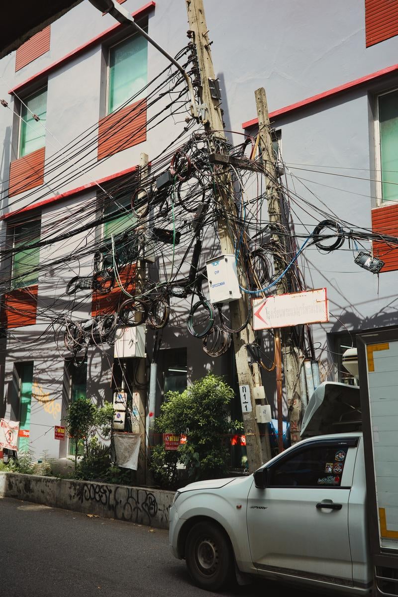 電柱に絡み合う複数の黒い電線と配線、赤い屋根の建物背景