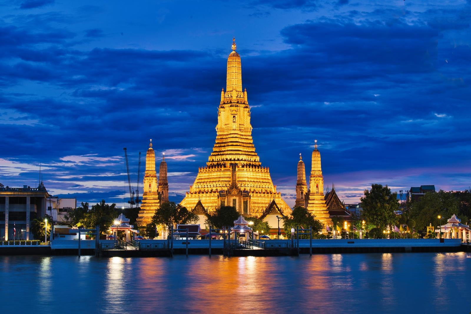 夜にオレンジ色にライトアップされたワット・アルンの仏塔群とチャオプラヤー川