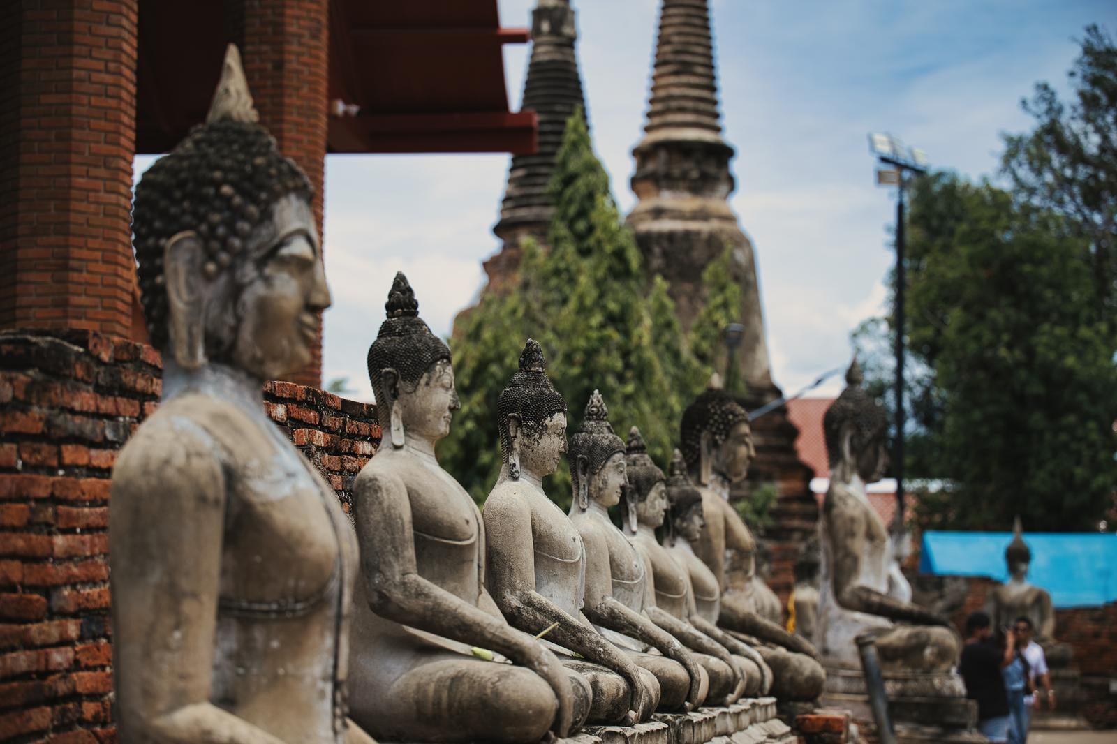 レンガ造りの仏塔を背景に石製の仏像が一列に並んでいる風景