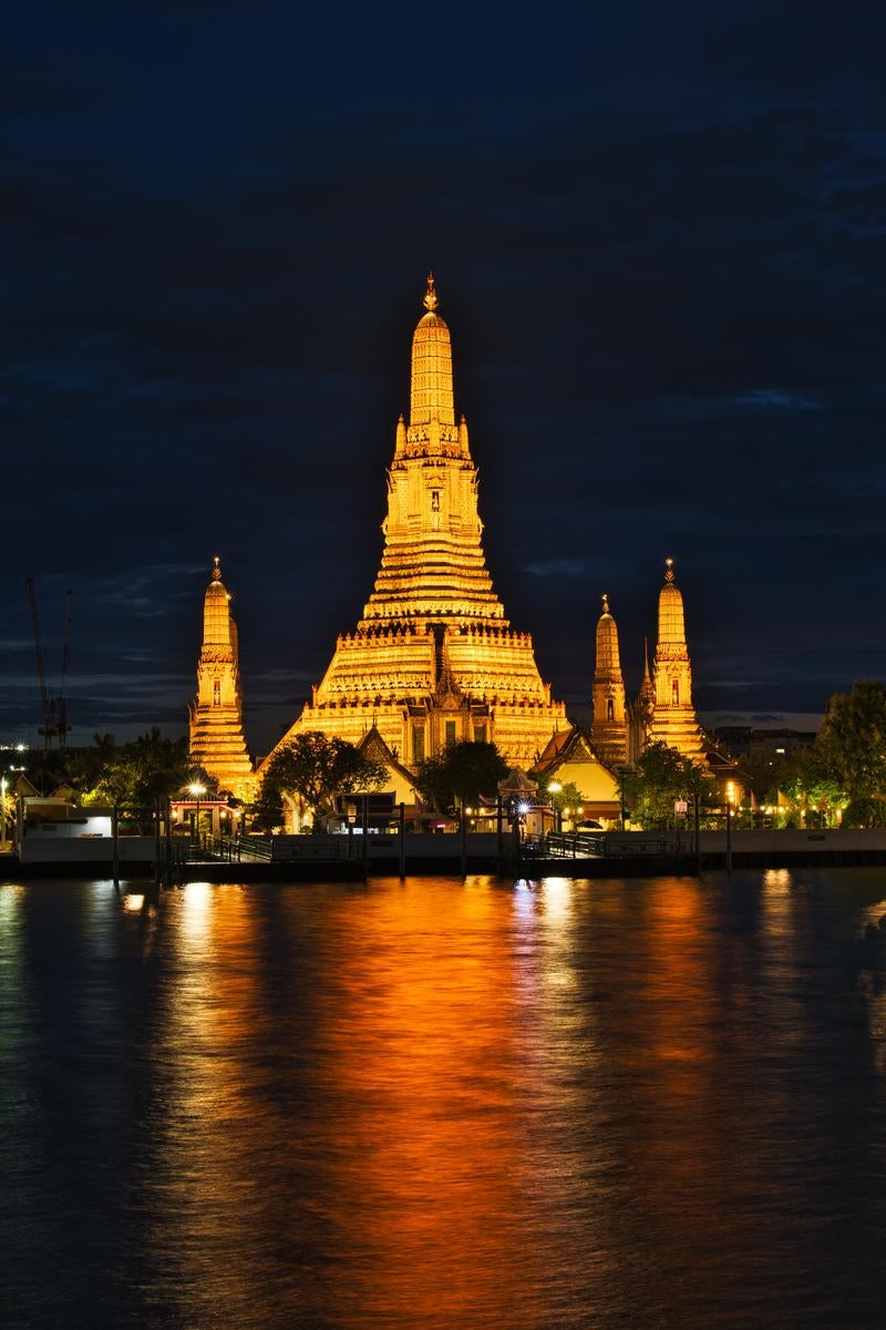 夜のチャオプラヤー川に映る黄金色にライトアップされたワットアルンの仏塔