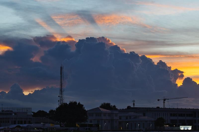 夕焼け空に立ち上がる巨大な積乱雲と都市の通信アンテナ