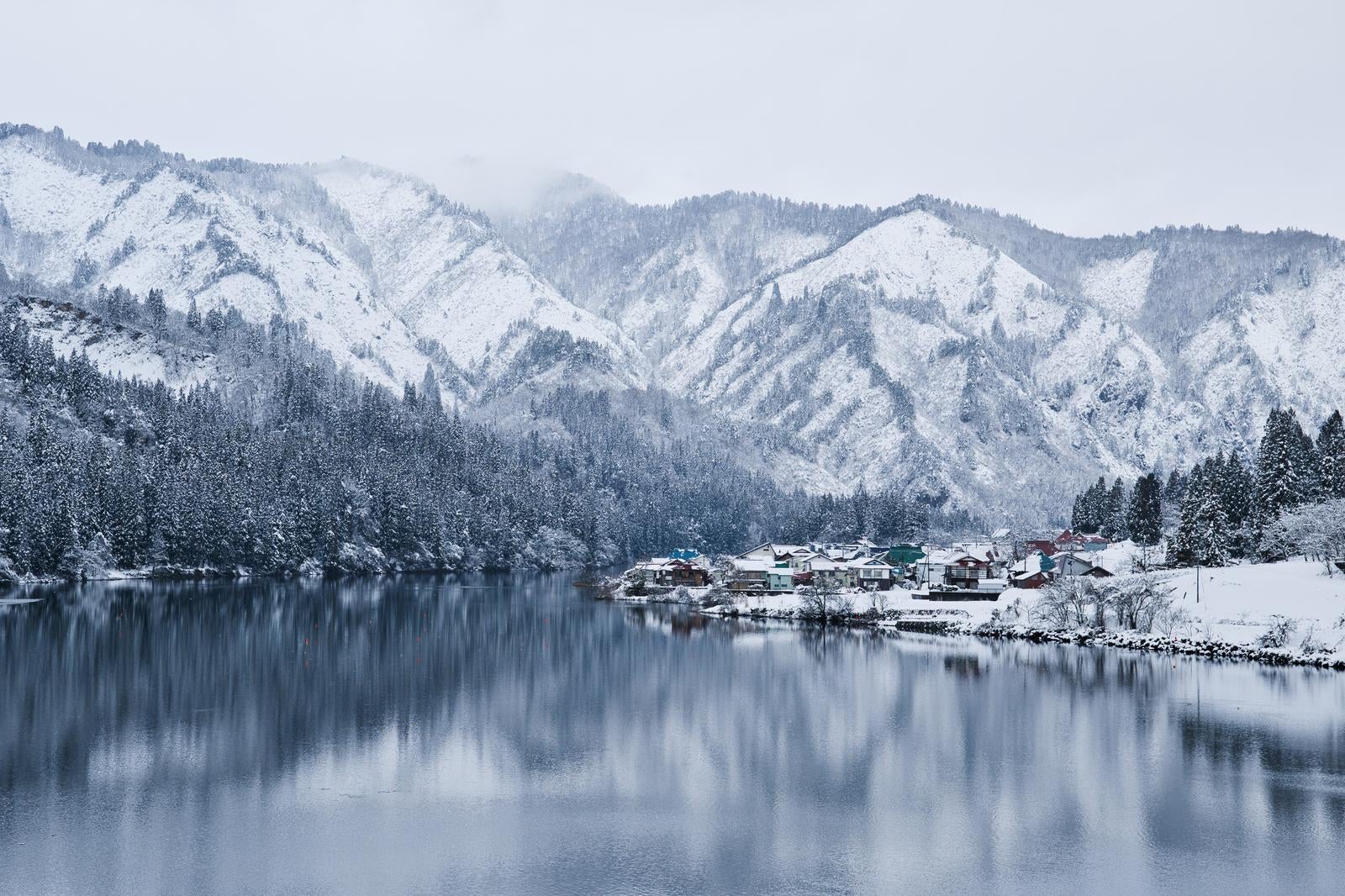 雪に覆われた山々を背景に、只見川沿いの雪景色に包まれた大志集落の冬の風景