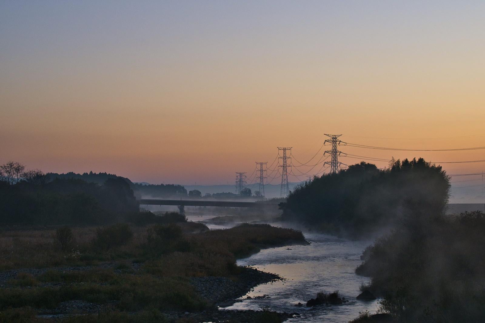 河川沿いに立つ送電線鉄塔と朝焼けの空の風景