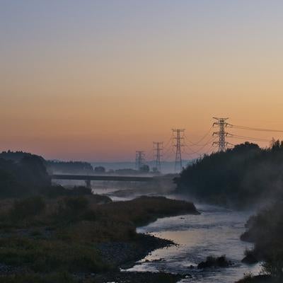 河川沿いの自然に囲まれた送電線鉄塔群の夜明けの風景の写真