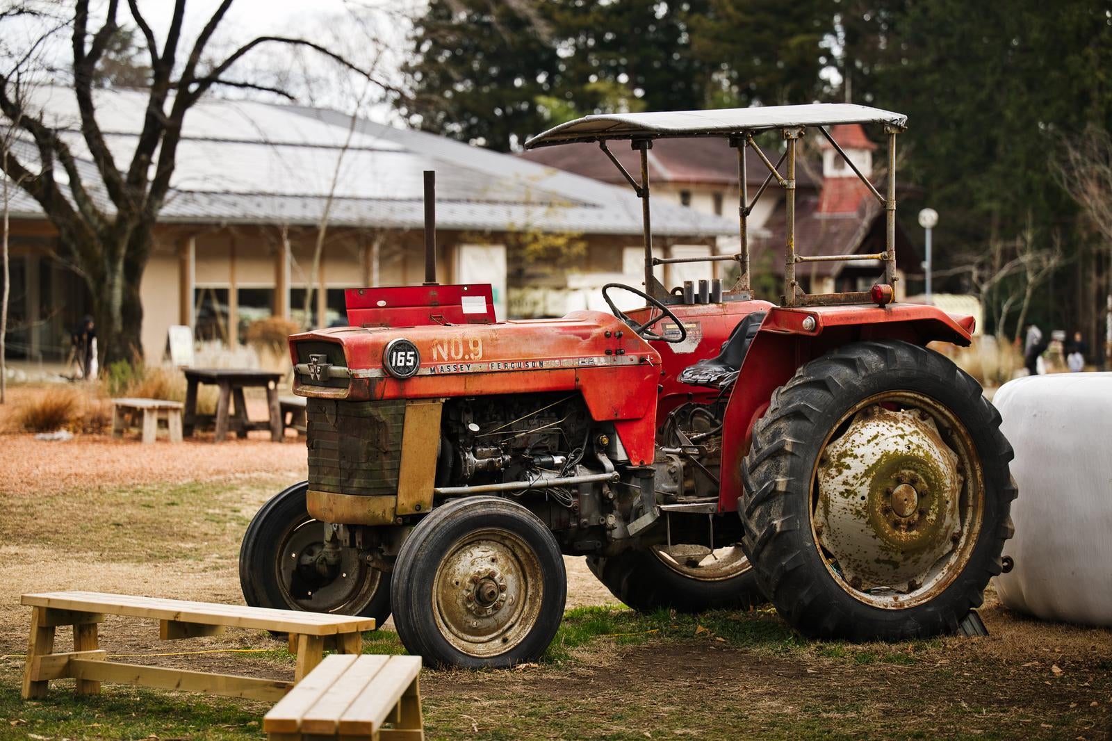 赤いトラクターが農場に停車しており、手前に木製ベンチがある