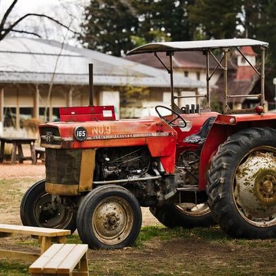 古い農場跡地に放置された赤いトラクターと木製のベンチの写真